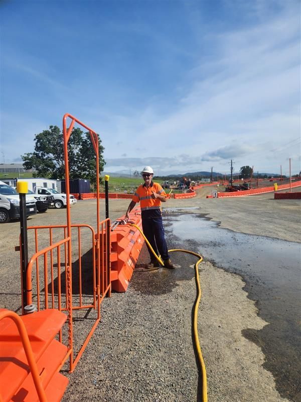 A Man in a Hard Hat is Standing Holding A Hose Which is Filling Orange Barricade — Hinterland Water Cartage in Mooloolah Valley, QLD