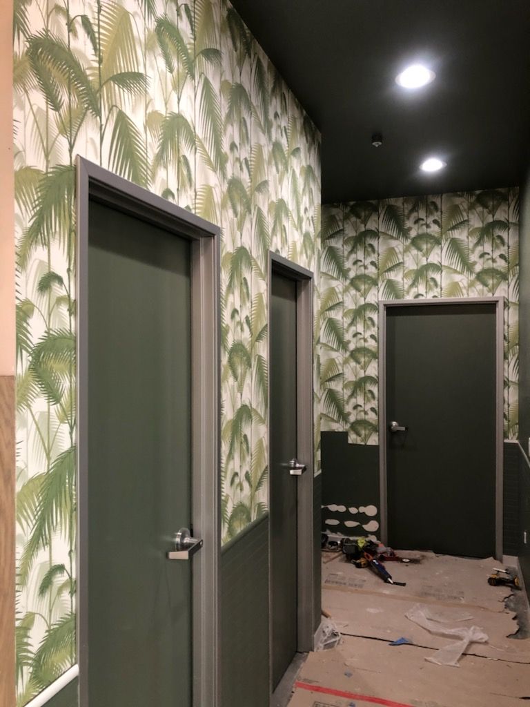 A hallway with green doors and tropical wallpaper on the walls.