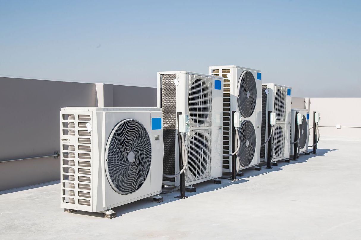 Outdoor row of white HVAC condenser units on a flat rooftop under a clear sky