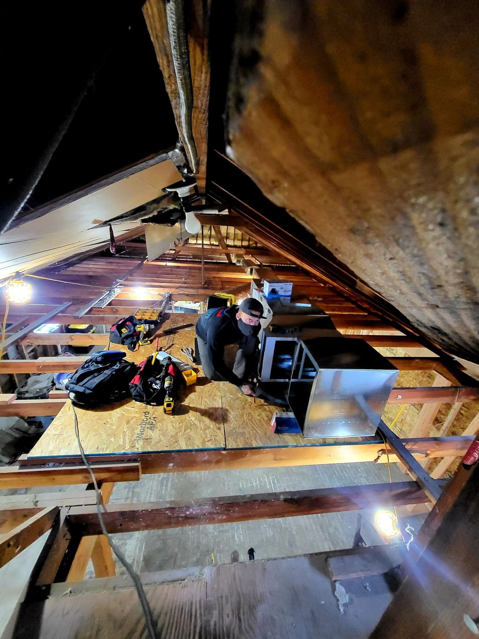 A man is working on a ventilation system in an attic.