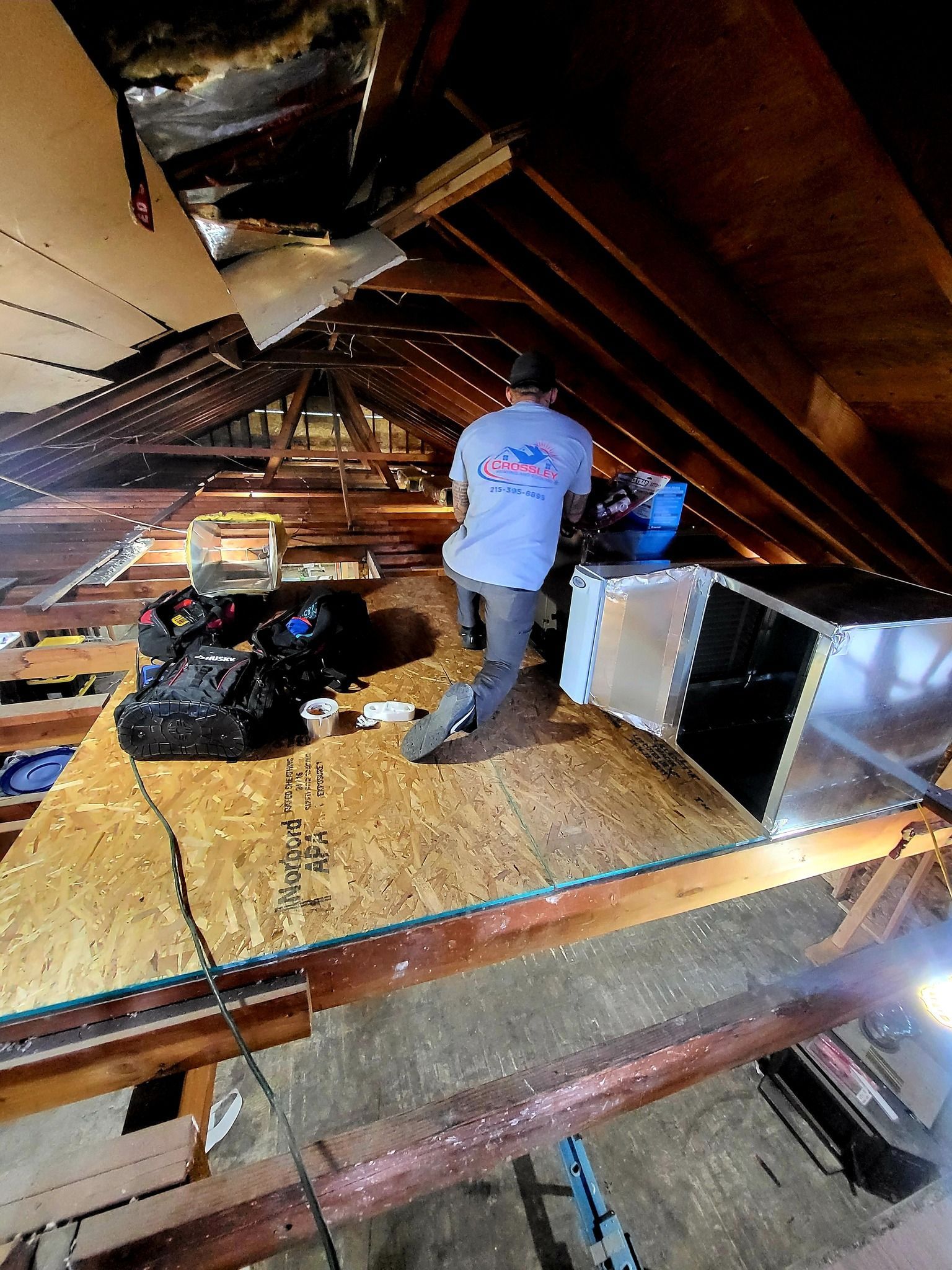 A man is working on an air duct in an attic.