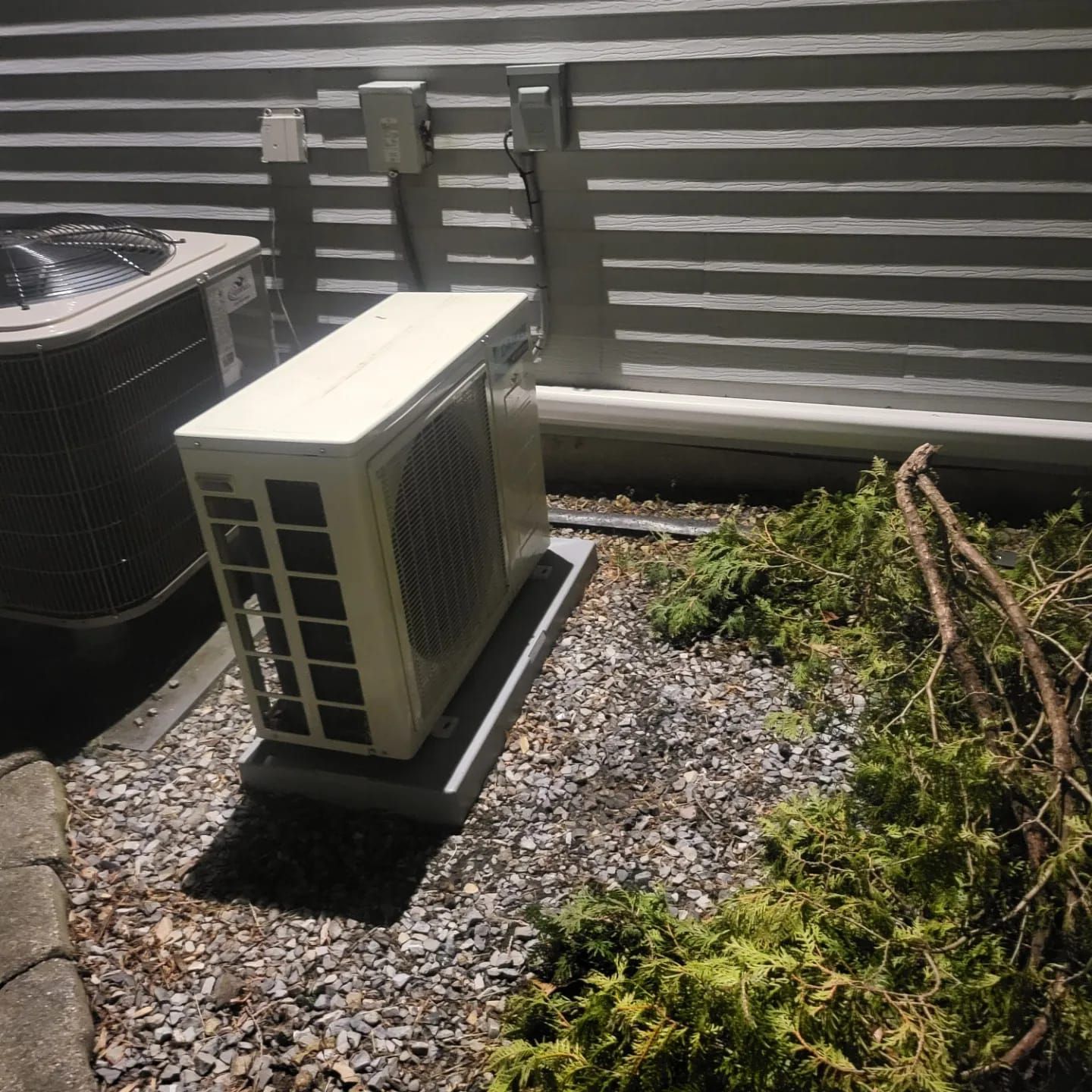 A white air conditioner is sitting on top of a pile of gravel.