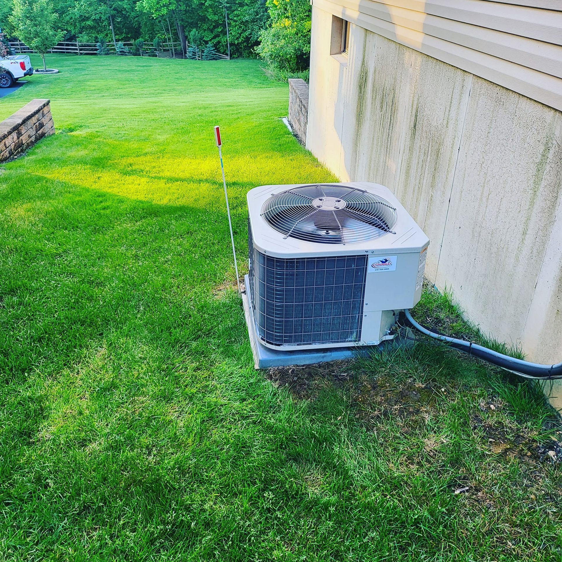 An air conditioner is sitting in the grass next to a house.