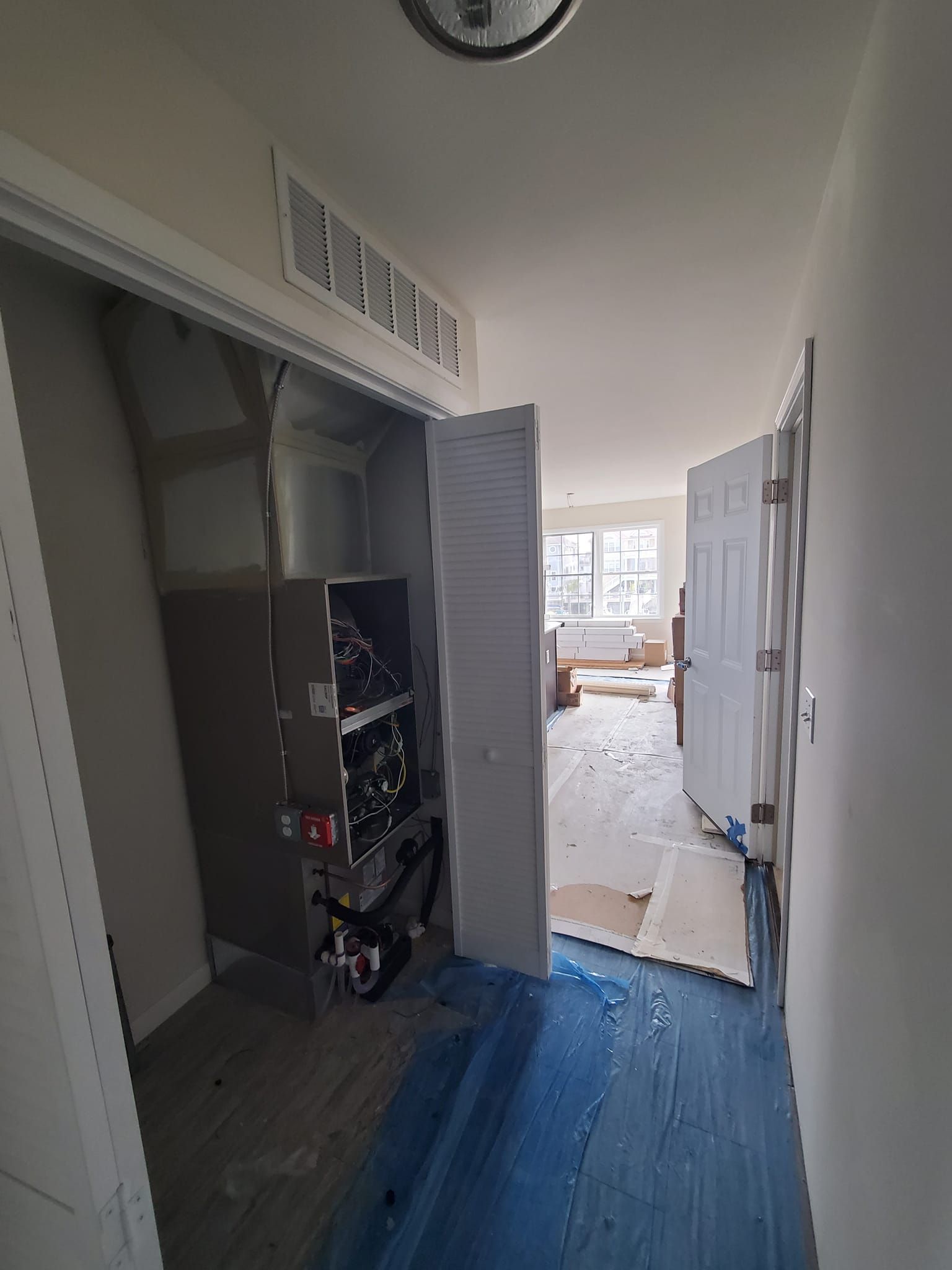 A hallway with a blue tarp on the floor leading to a living room.