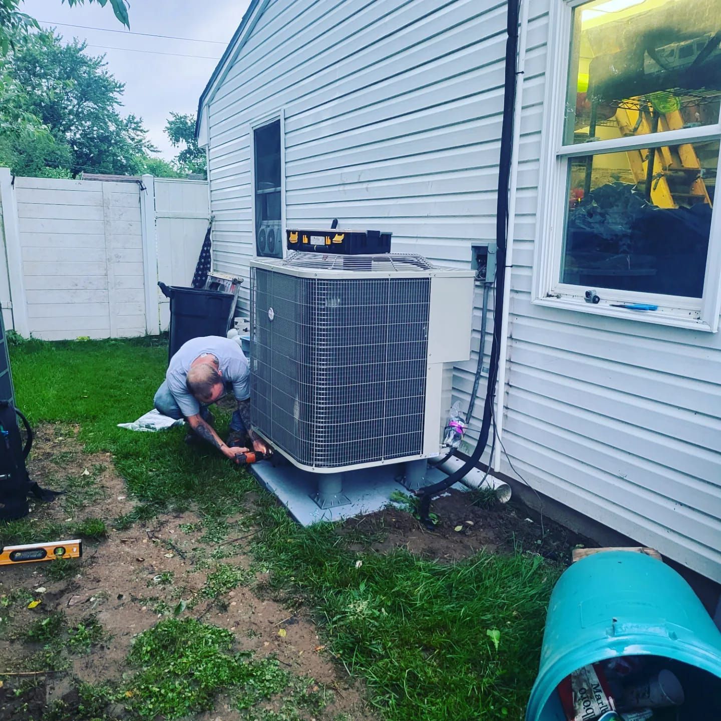 A man is working on an air conditioner in the backyard of a house.