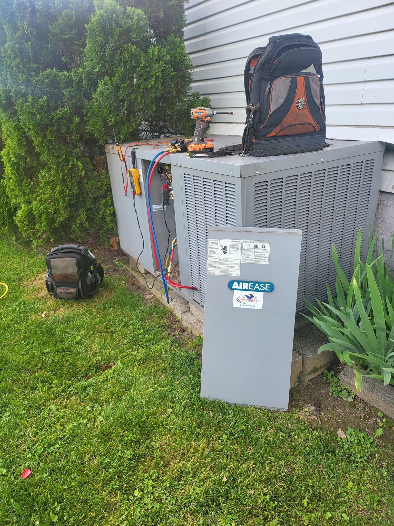 An air conditioner is being repaired in the backyard of a house.