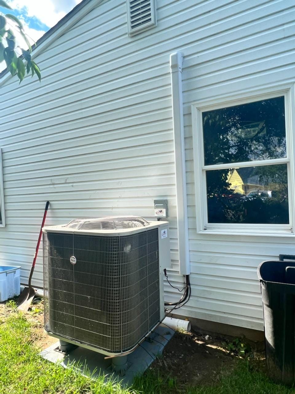 An air conditioner is sitting on the side of a house next to a window.