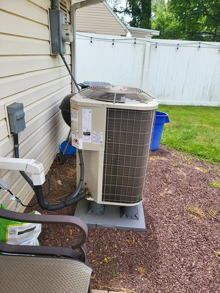 An air conditioner is sitting on the side of a house next to a chair.