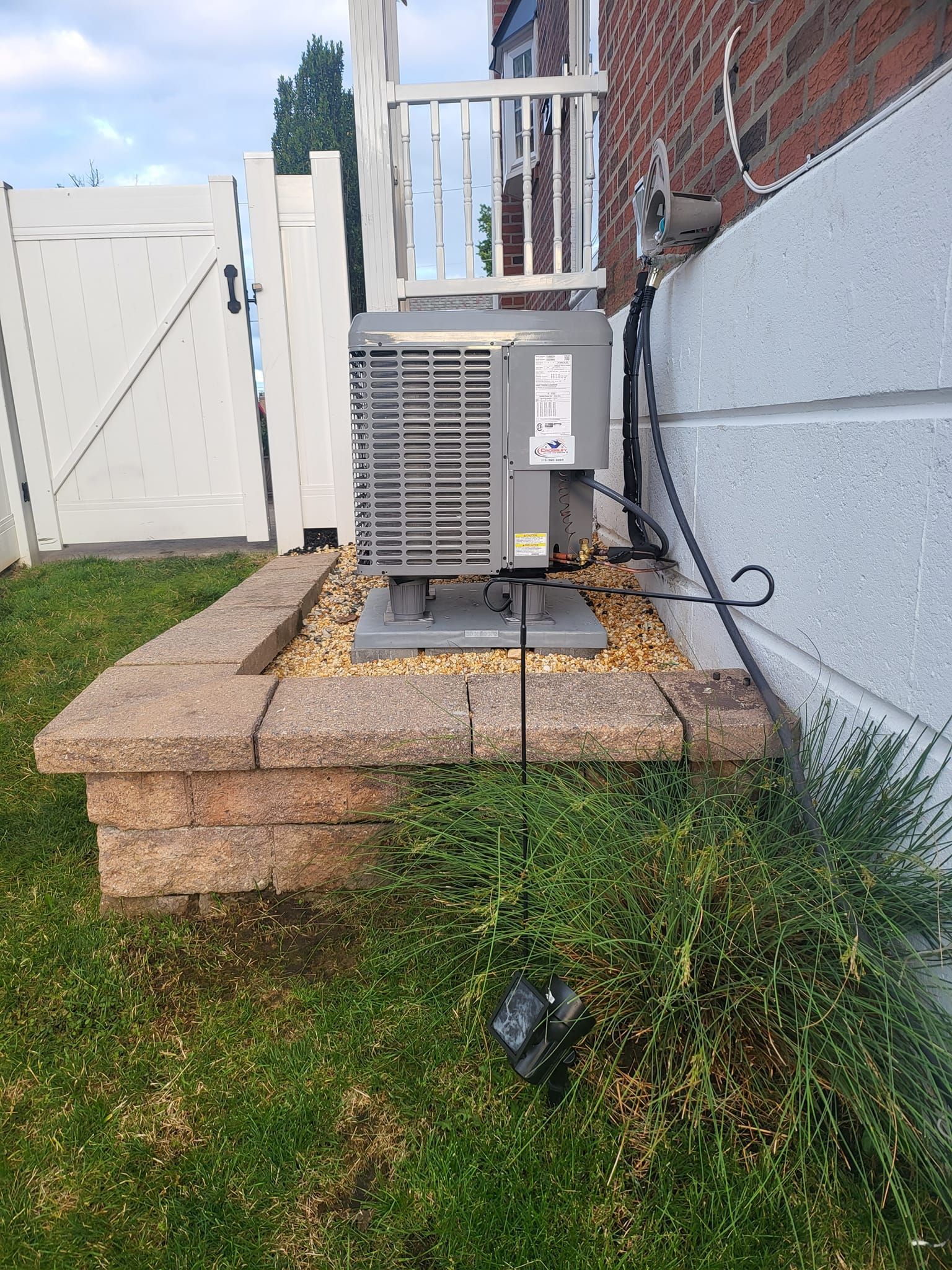 An air conditioner is sitting on top of a brick wall next to a fence.