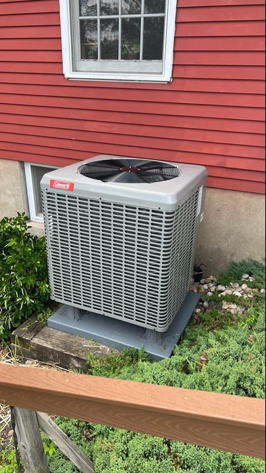 A large air conditioner is sitting outside of a red house.