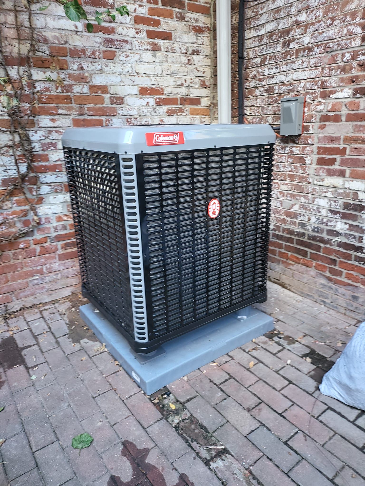 An air conditioner is sitting on a brick sidewalk next to a brick wall.