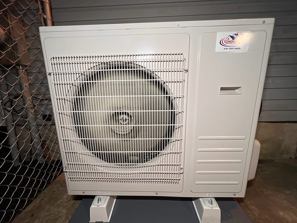 A large white air conditioner is sitting next to a chain link fence.