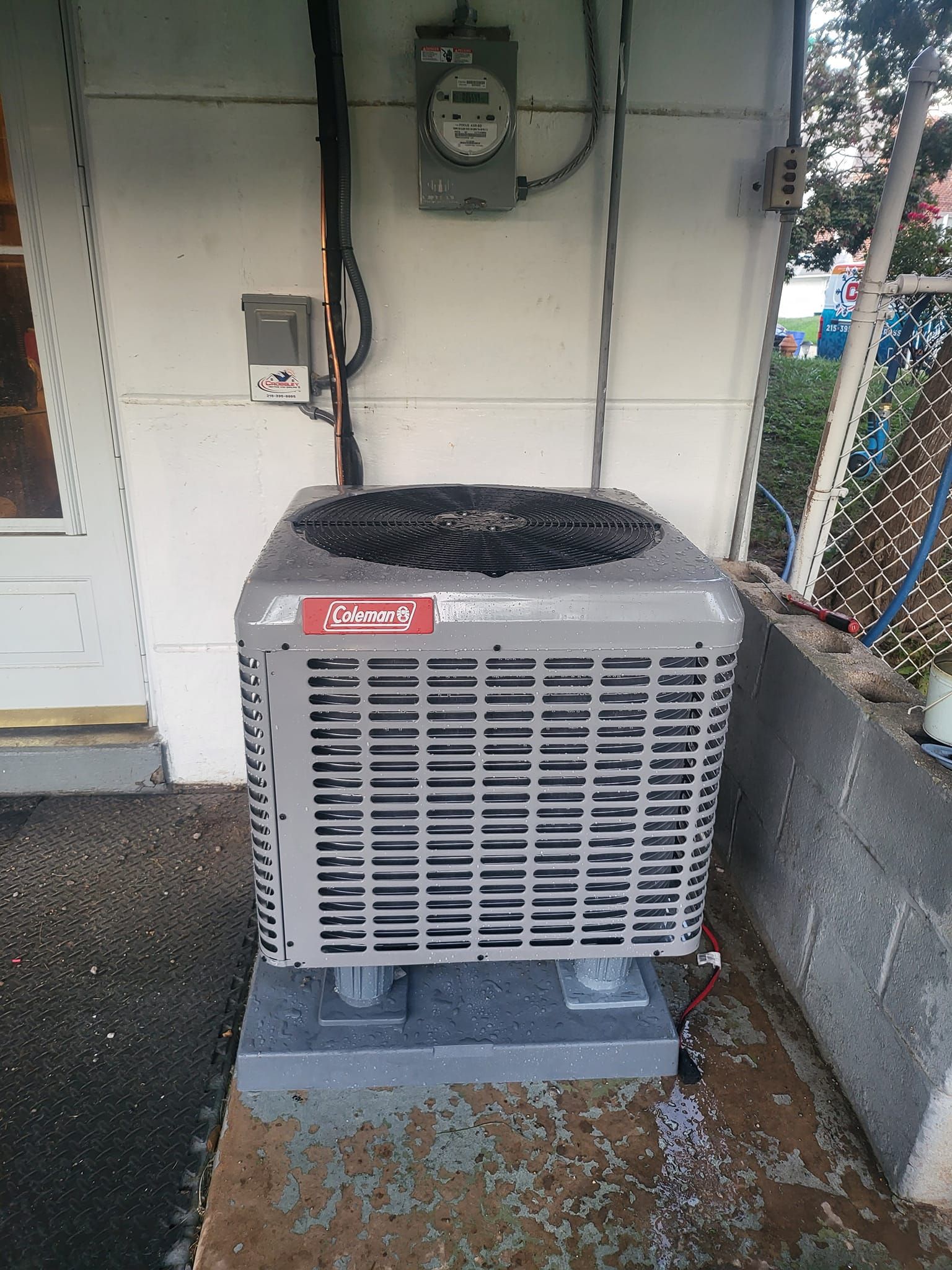 A gray air conditioner is sitting outside of a white building.