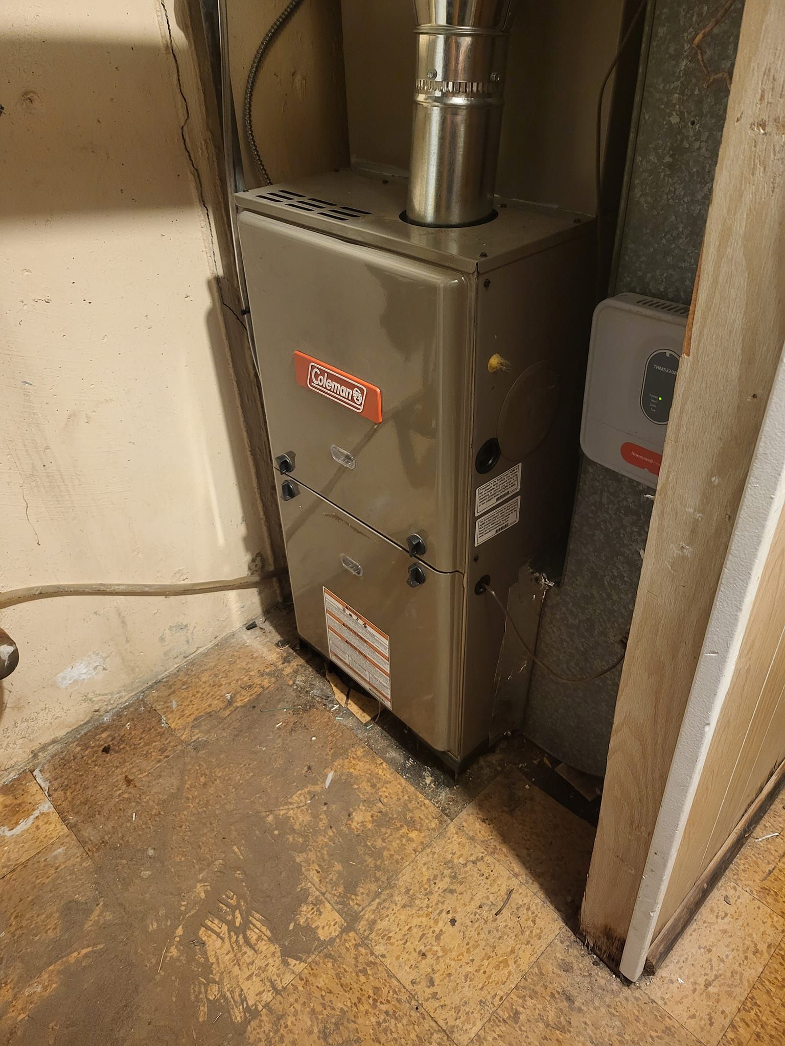 A furnace is sitting in a corner of a room next to a door.