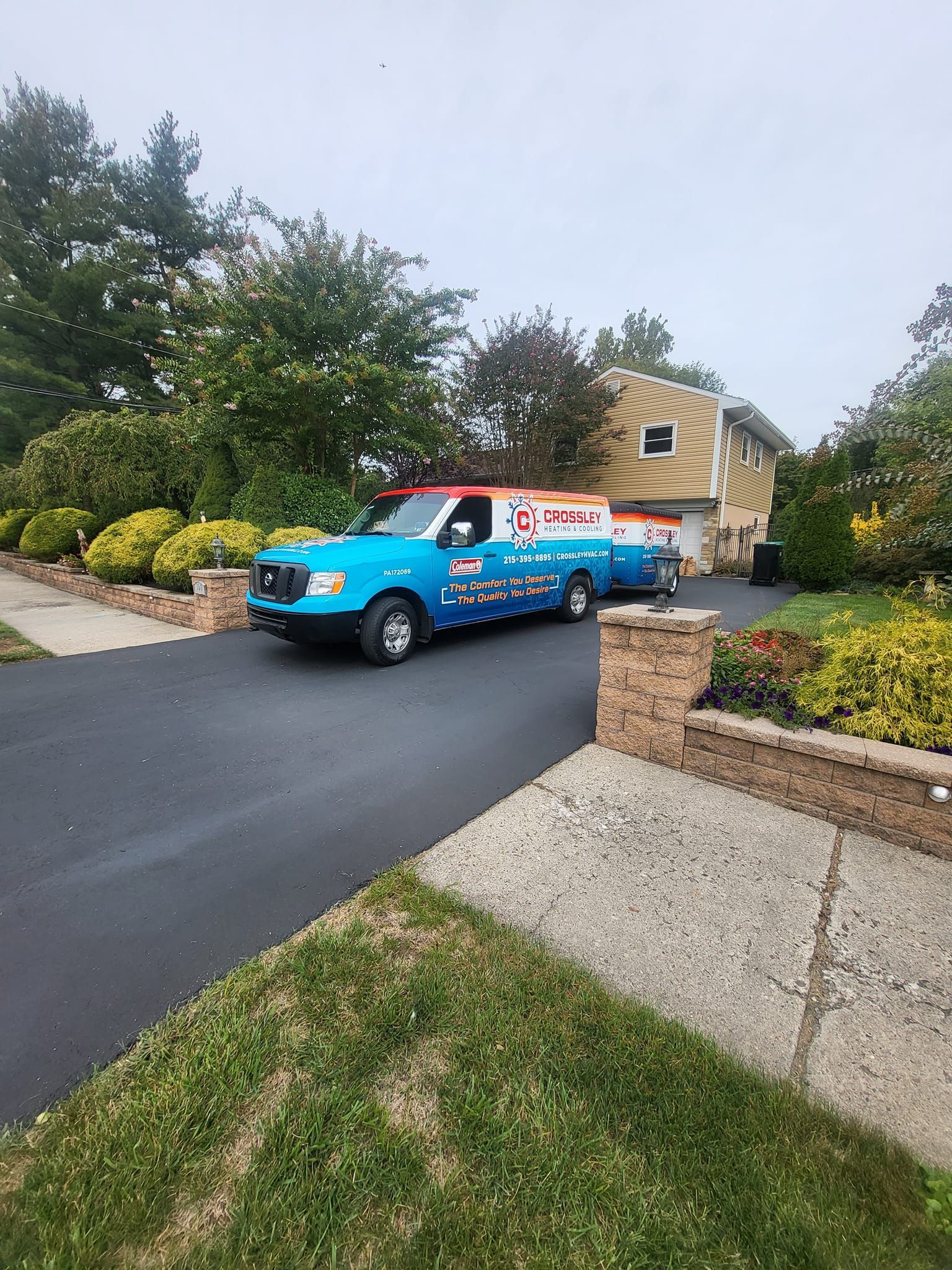 A blue and white van is driving down a street in front of a house.