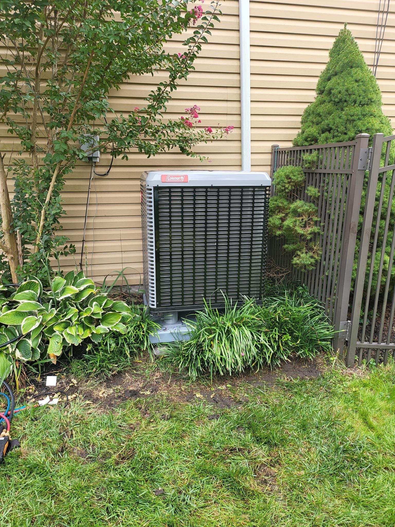 An air conditioner is sitting on the side of a house next to a fence.