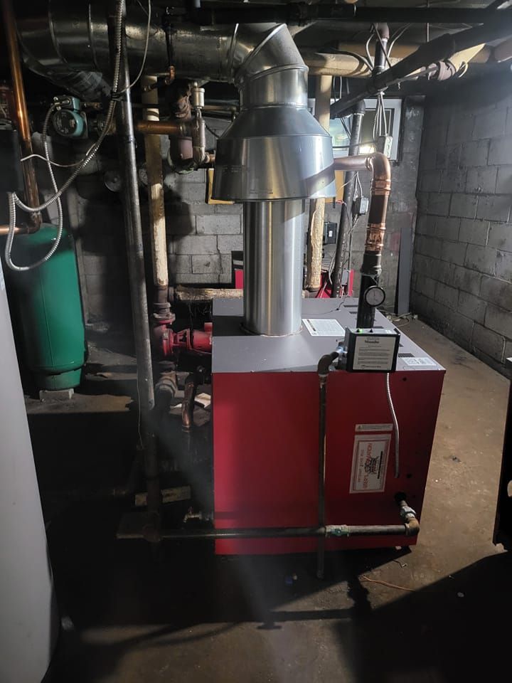 A red boiler is sitting in a basement next to a green tank.