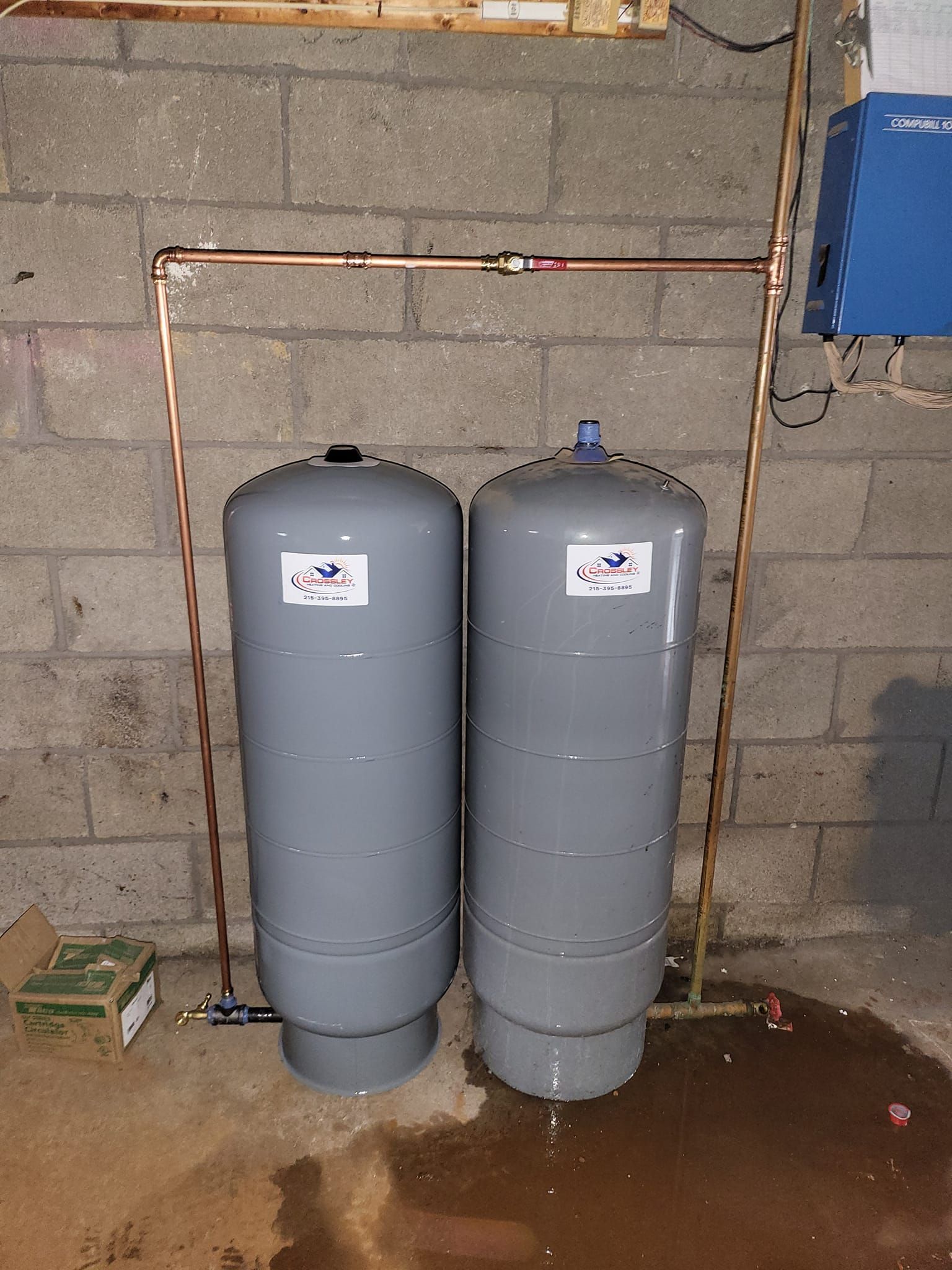 Two water tanks are sitting next to each other in a basement.