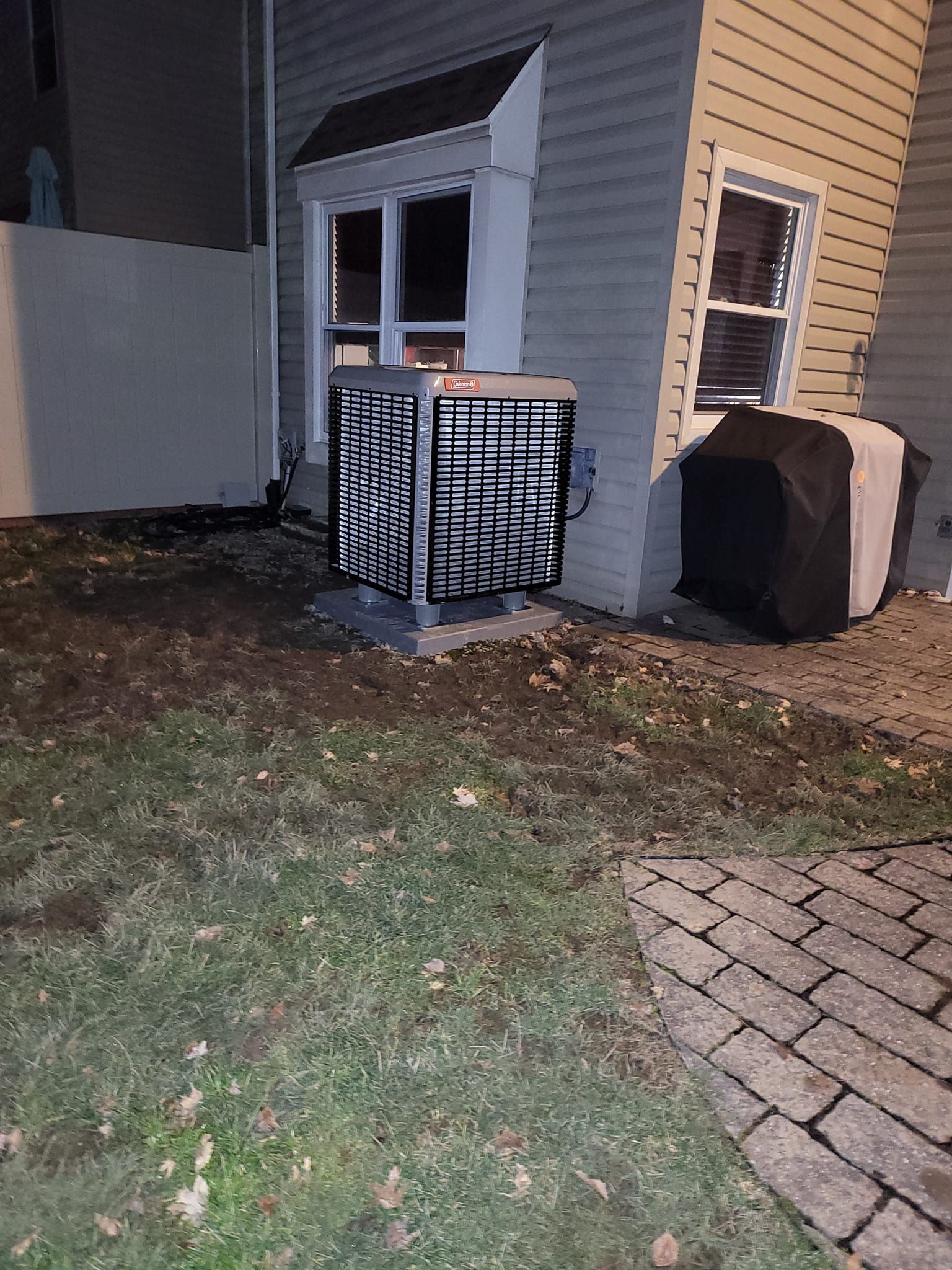 An air conditioner is sitting in the grass in front of a house.