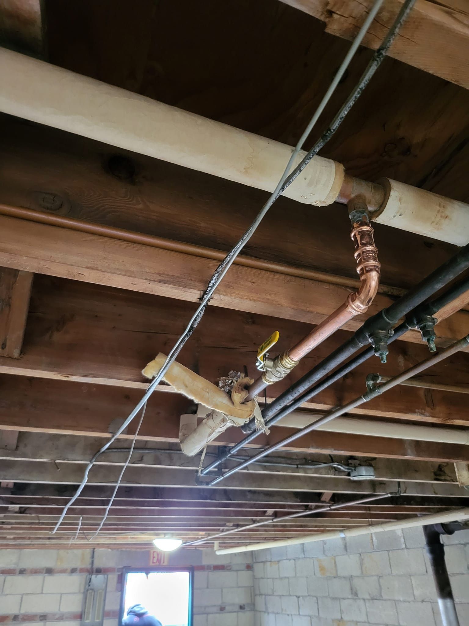 A bunch of pipes are hanging from the ceiling of a basement.