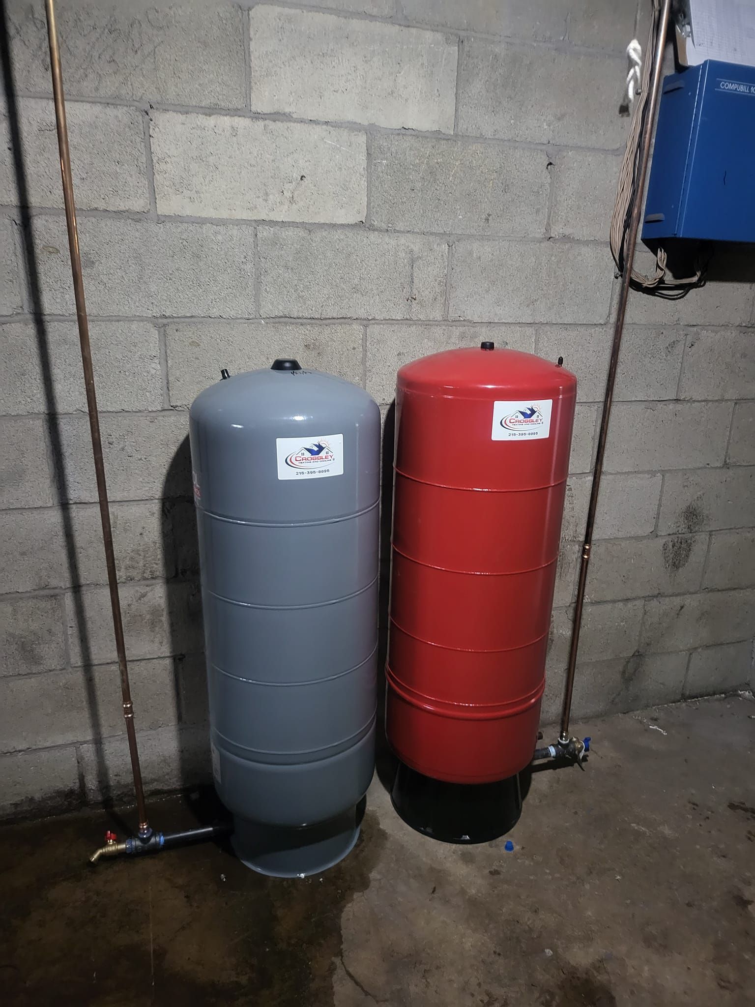 Two water tanks are sitting next to each other in a basement.