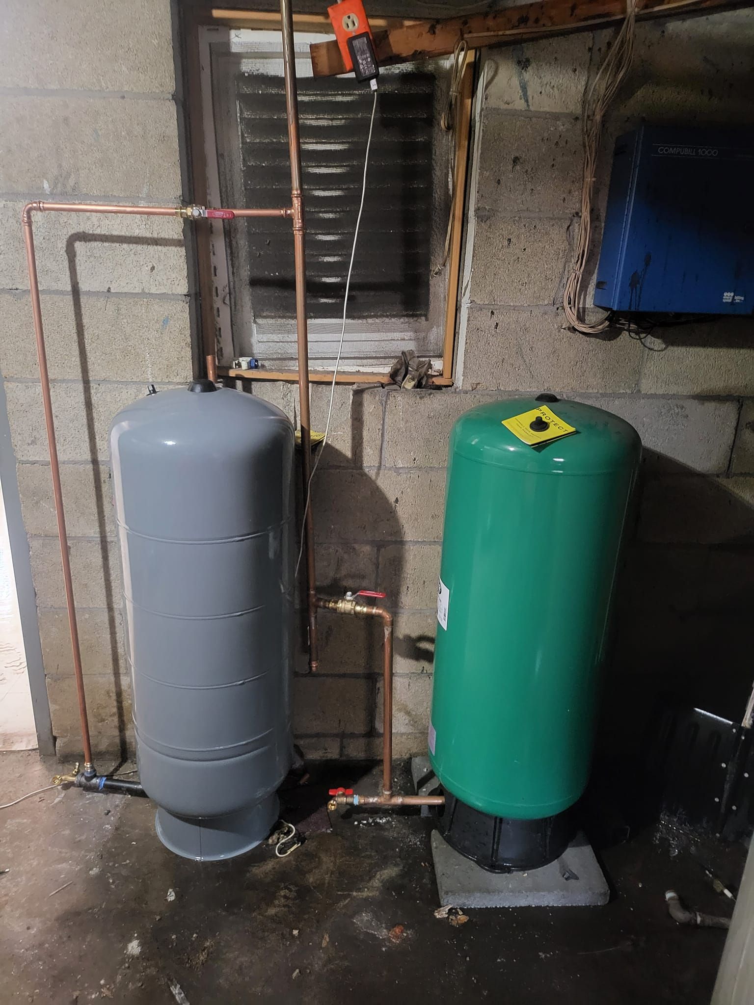 Two water tanks are sitting next to each other in a basement.
