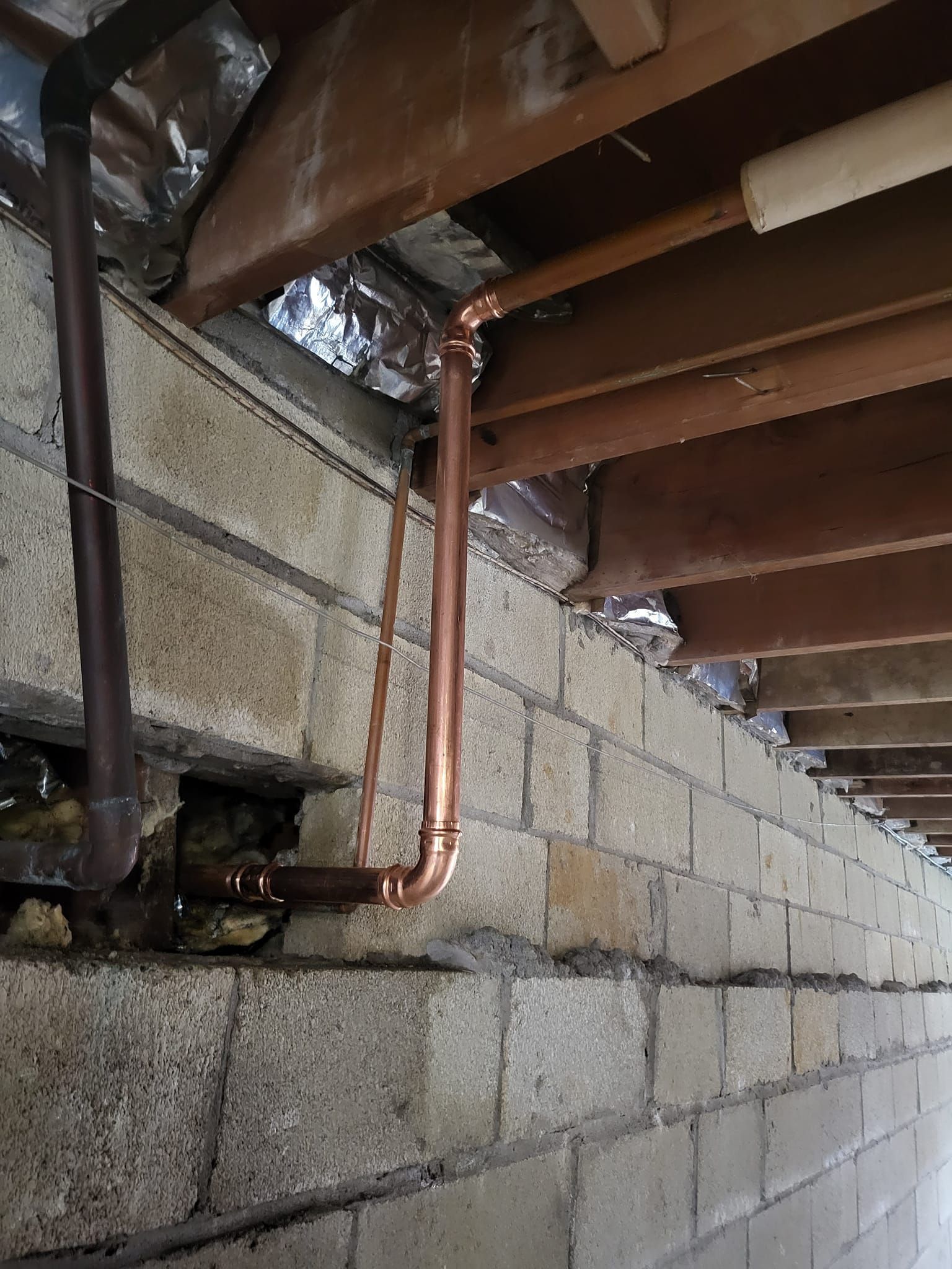 A copper pipe is hanging from the ceiling of a brick wall.