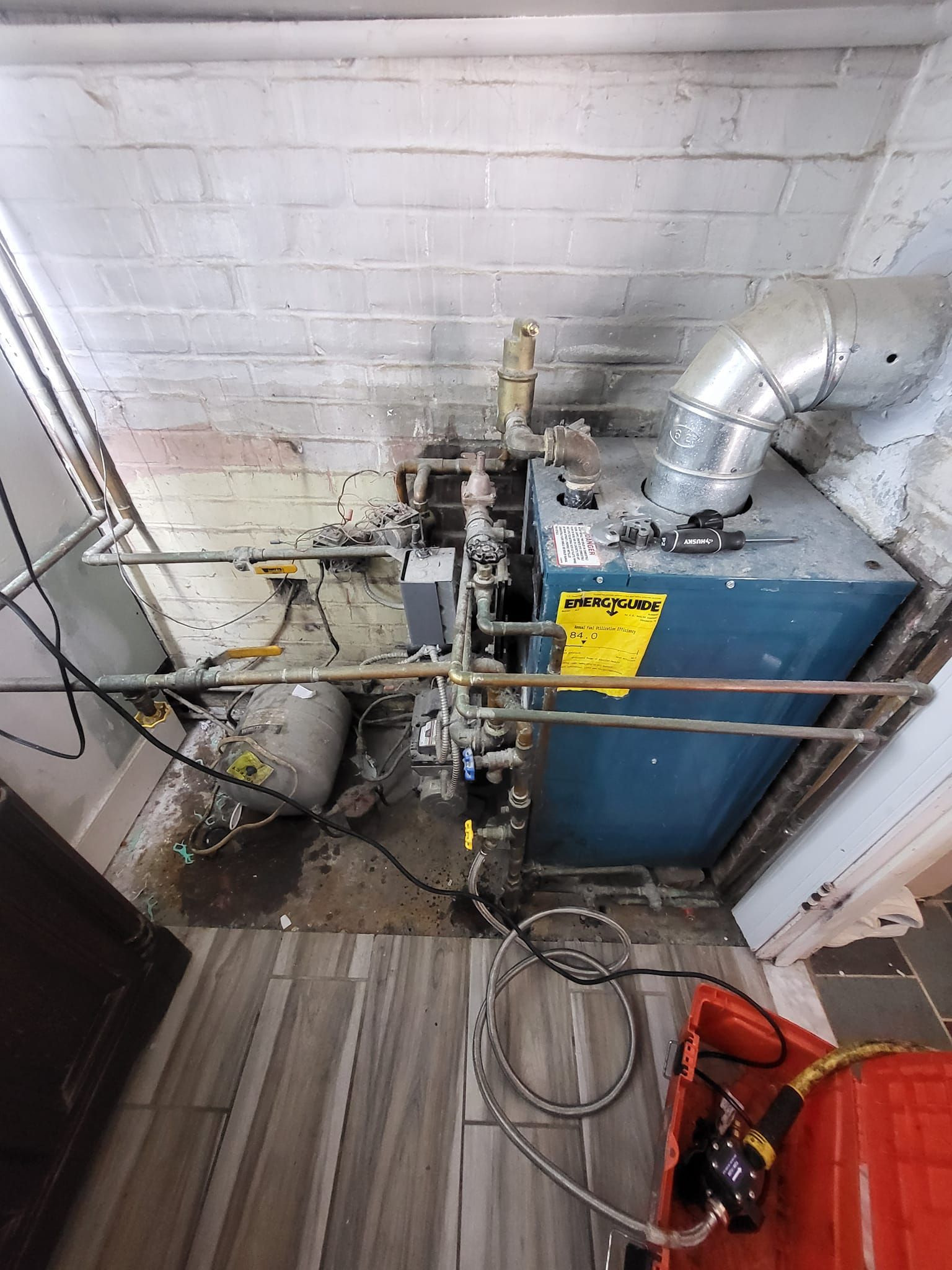 A blue boiler is sitting in a room next to a brick wall.