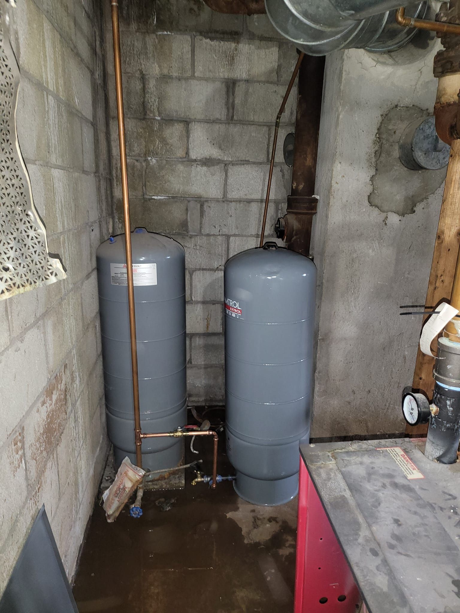 Two water tanks are sitting in a basement next to a brick wall.