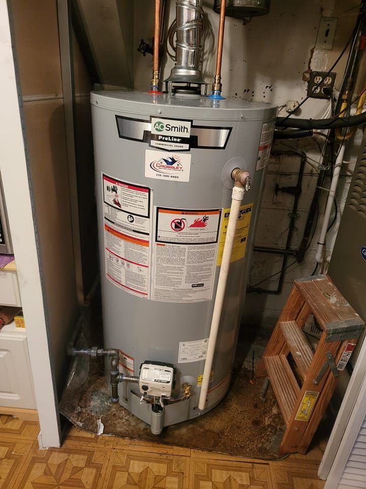 A water heater is sitting in a corner of a room next to a ladder.