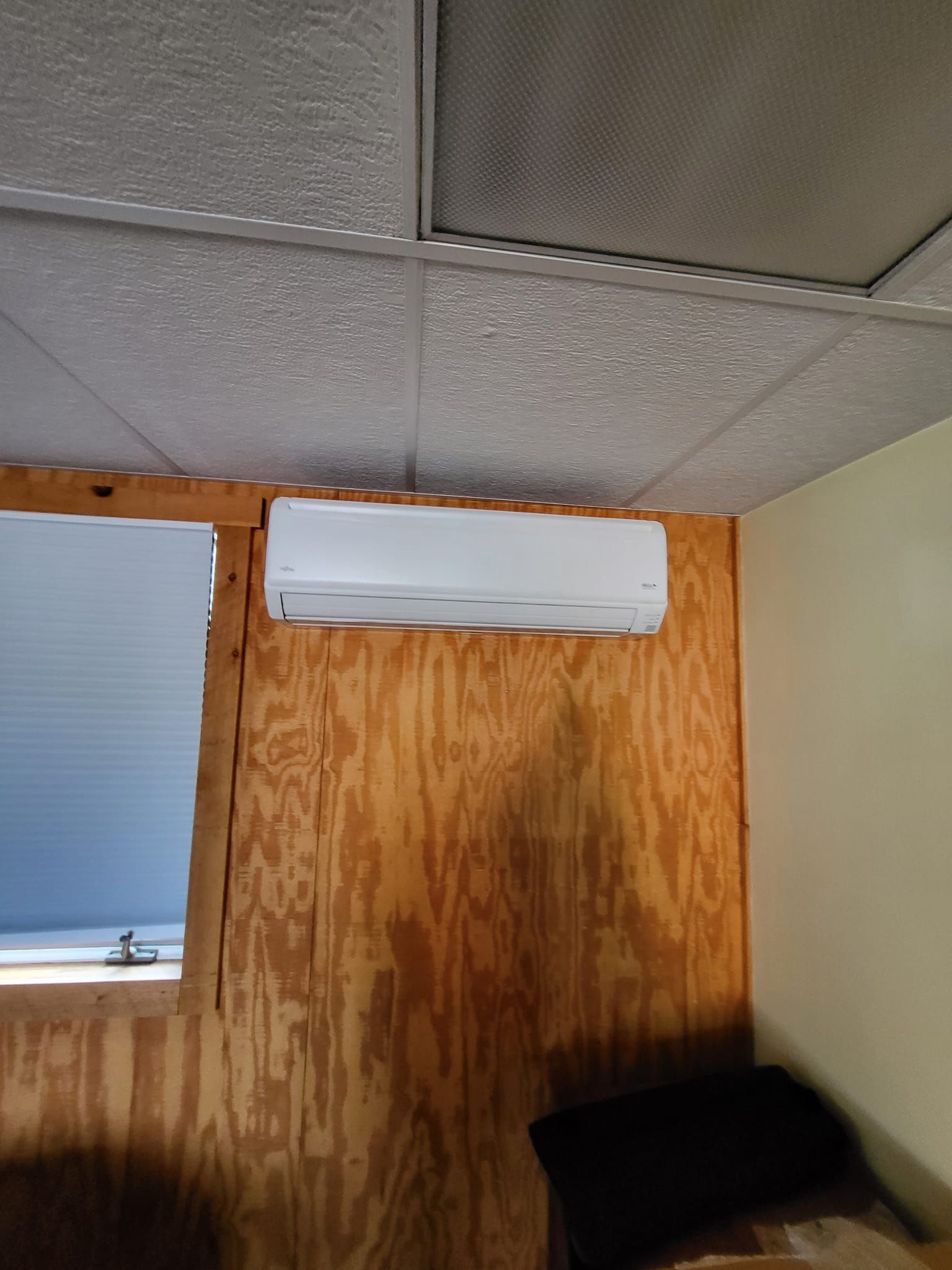 A room with a window and a white air conditioner hanging from the ceiling.