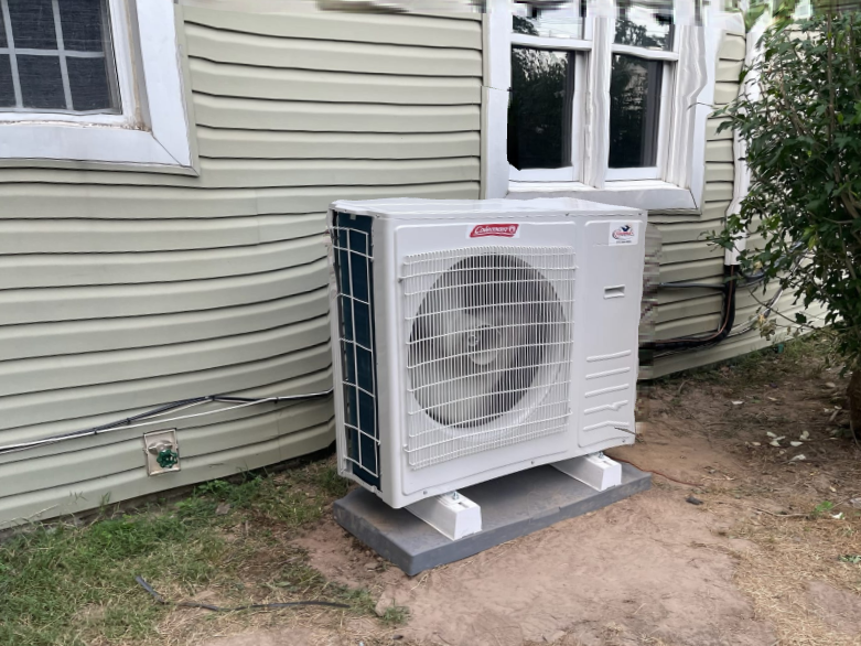 A large white air conditioner is sitting outside of a house.