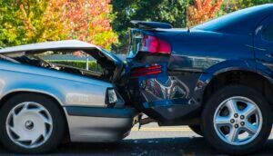 Two cars involved in a rear-end collision on a road; one blue, one silver.