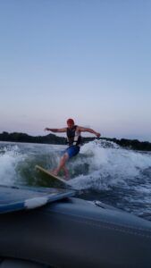 Person wake surfing on a wave, arms out, wearing a life vest. Dark water and sky.