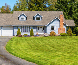 Blue house with gray roof, brick chimney, garage, and lush green lawn.