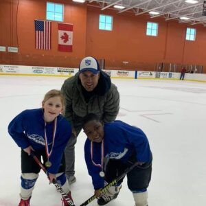 Two children and a man pose on an ice rink, wearing hockey jerseys and medals.
