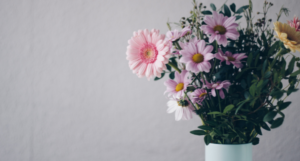 Bouquet of pink and white flowers in a light blue vase against a neutral wall.
