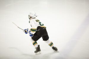 Hockey player skating on ice, wearing a white jersey with green and black accents.