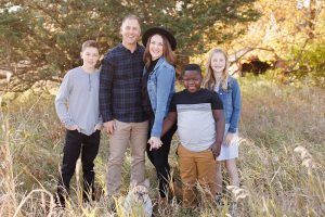 Family of five posing outdoors in tall grass, smiling.