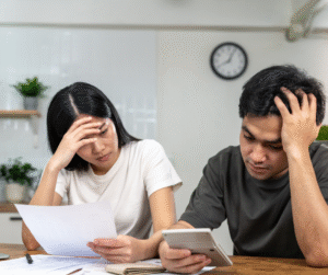 Couple reviewing bills, looking stressed, using a calculator at a table.