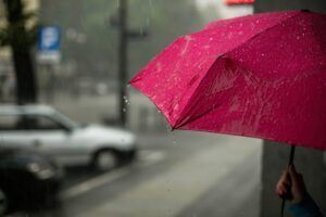 Pink umbrella in the rain on a city street, partially obscuring cars.