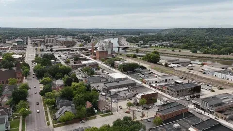 Aerial view of a town with buildings, roads, and a river in the background under a cloudy sky.