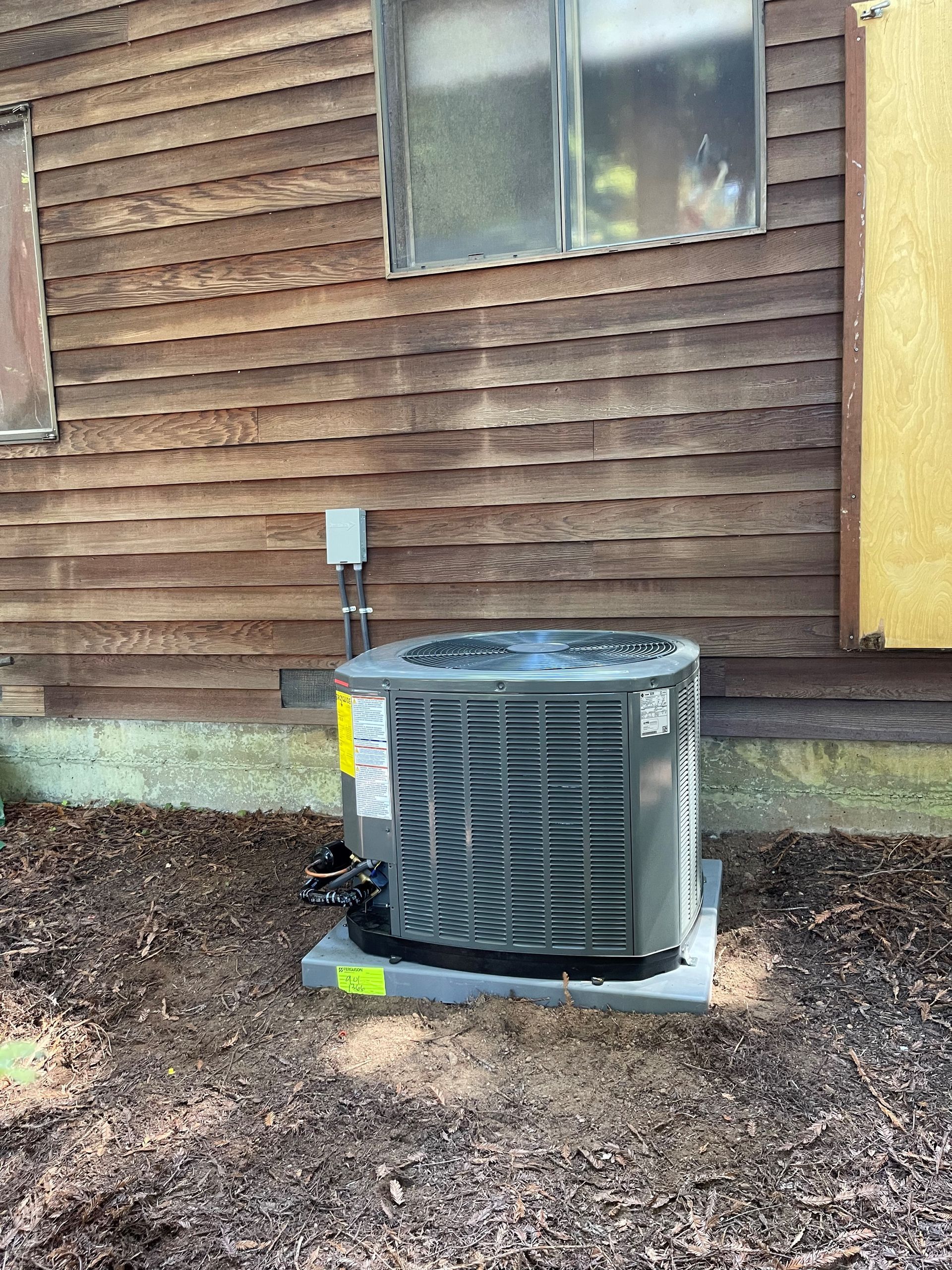 An air conditioner is sitting on the side of a wooden house.
