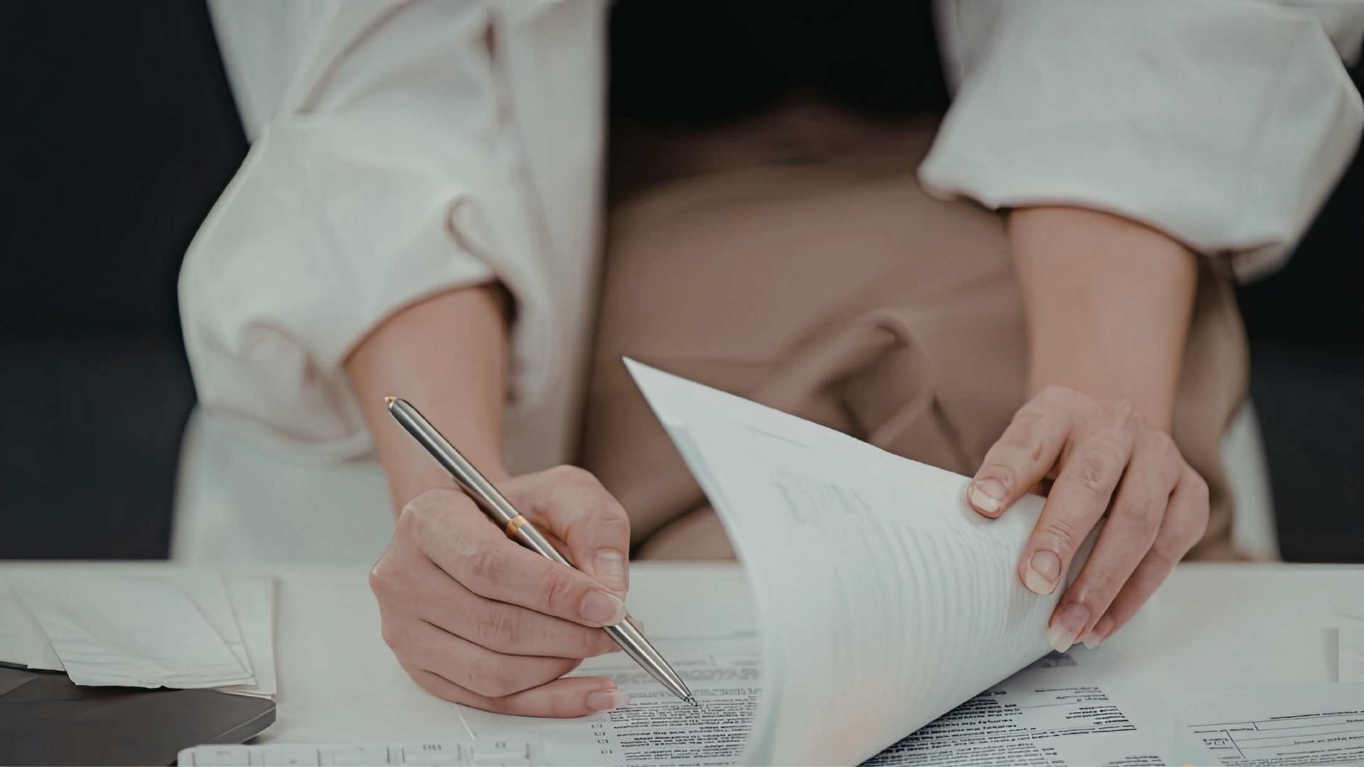 Hands writing in a notebook with a pen beside a turned book on a desk