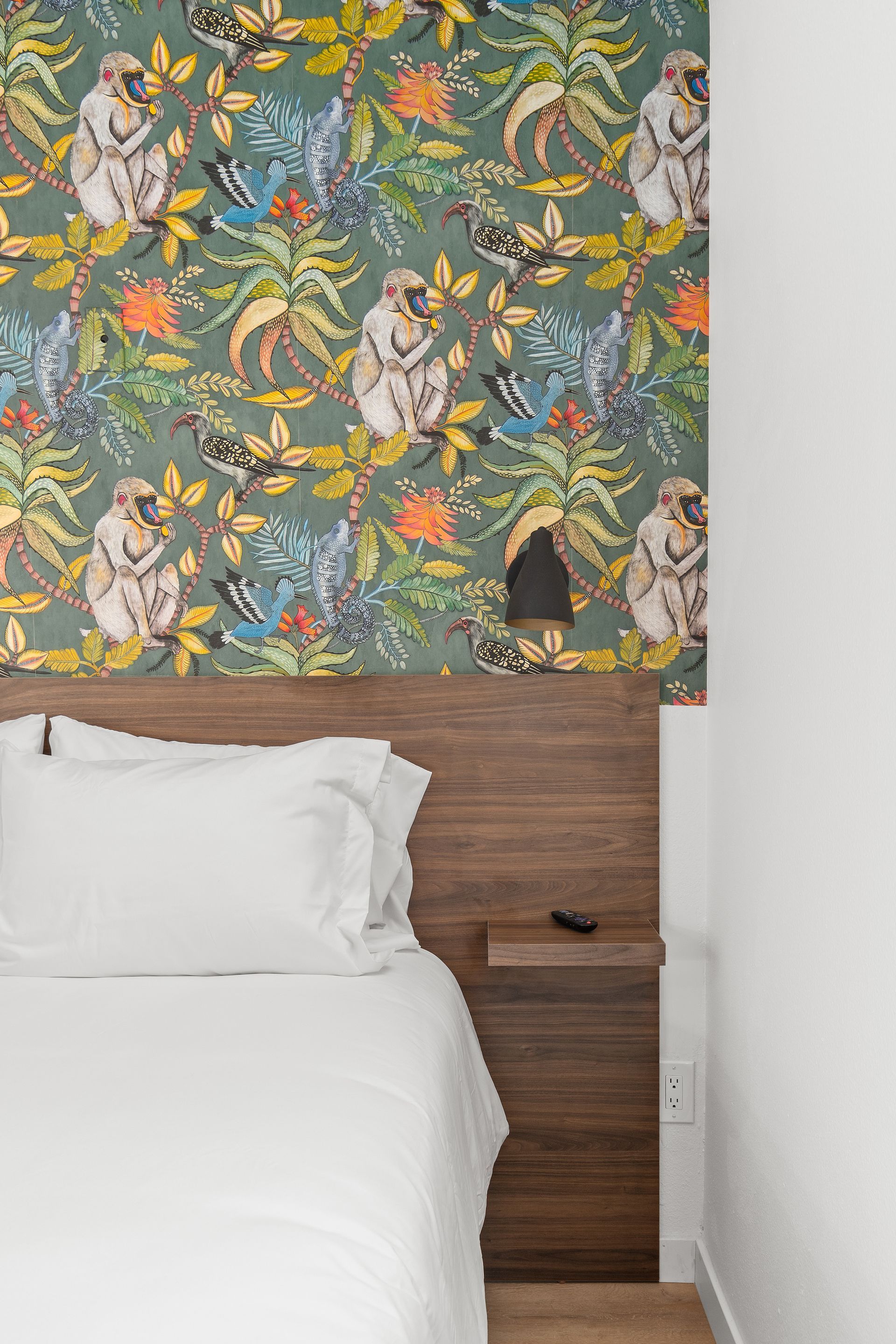 A bedroom with a bed , nightstand , and wallpaper with monkeys on it.