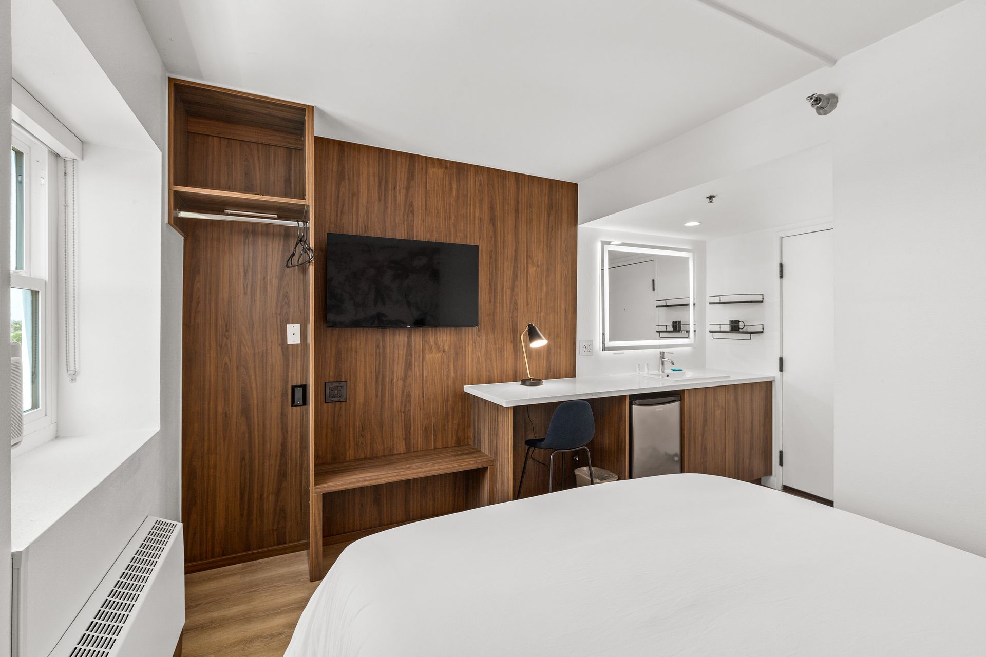 A hotel room with a bed , desk , television and mirror.