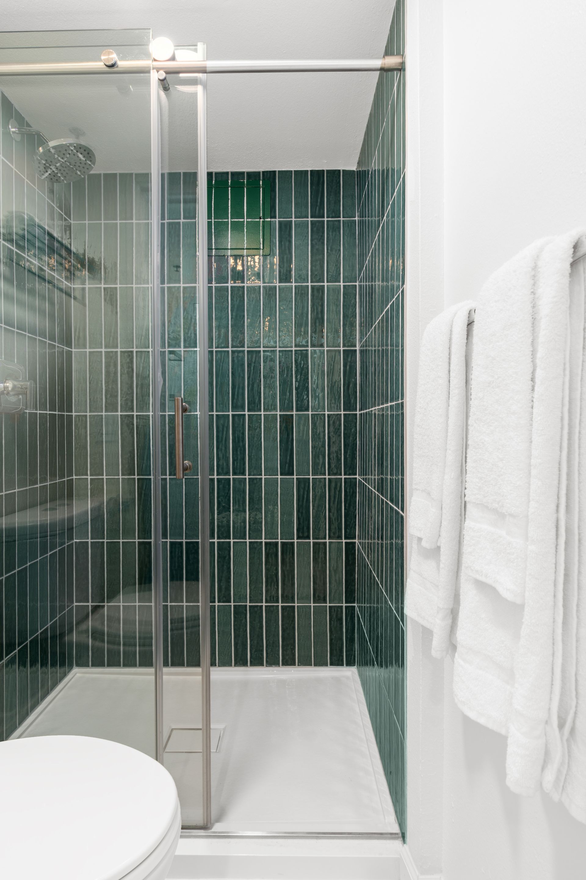 A bathroom with green tiles , a toilet , and a walk in shower.