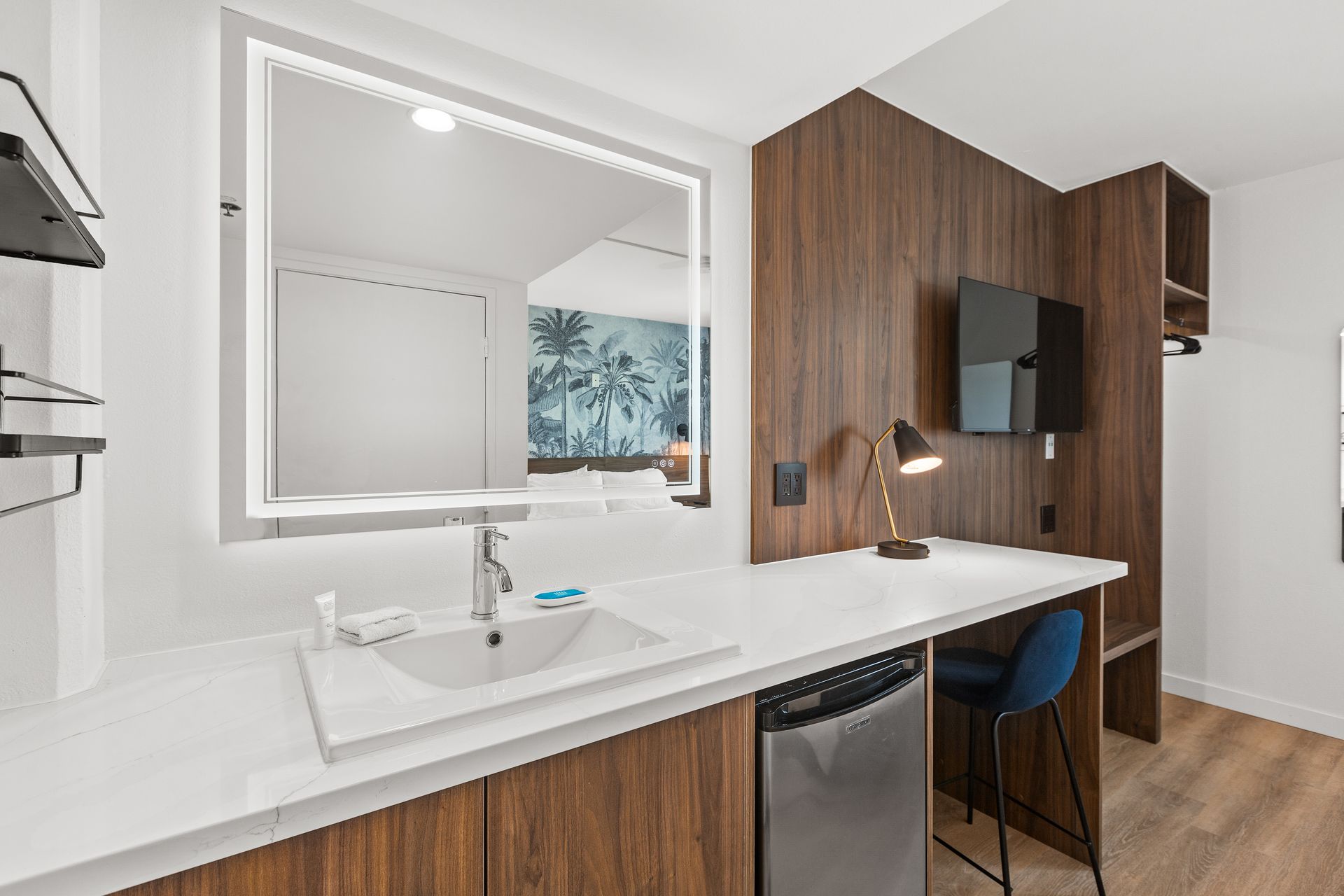 A hotel room with a sink , desk , television and mirror.