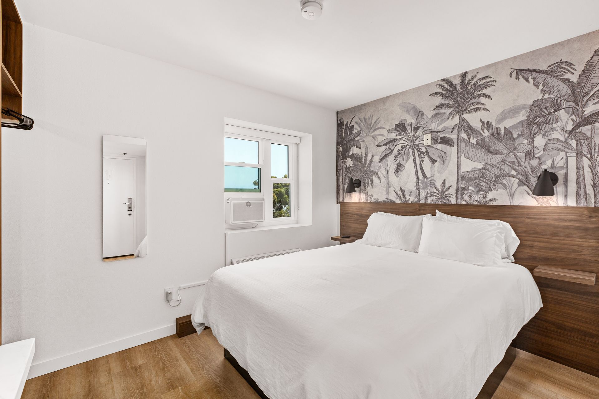 A hotel room with a king size bed , a mirror and a window.