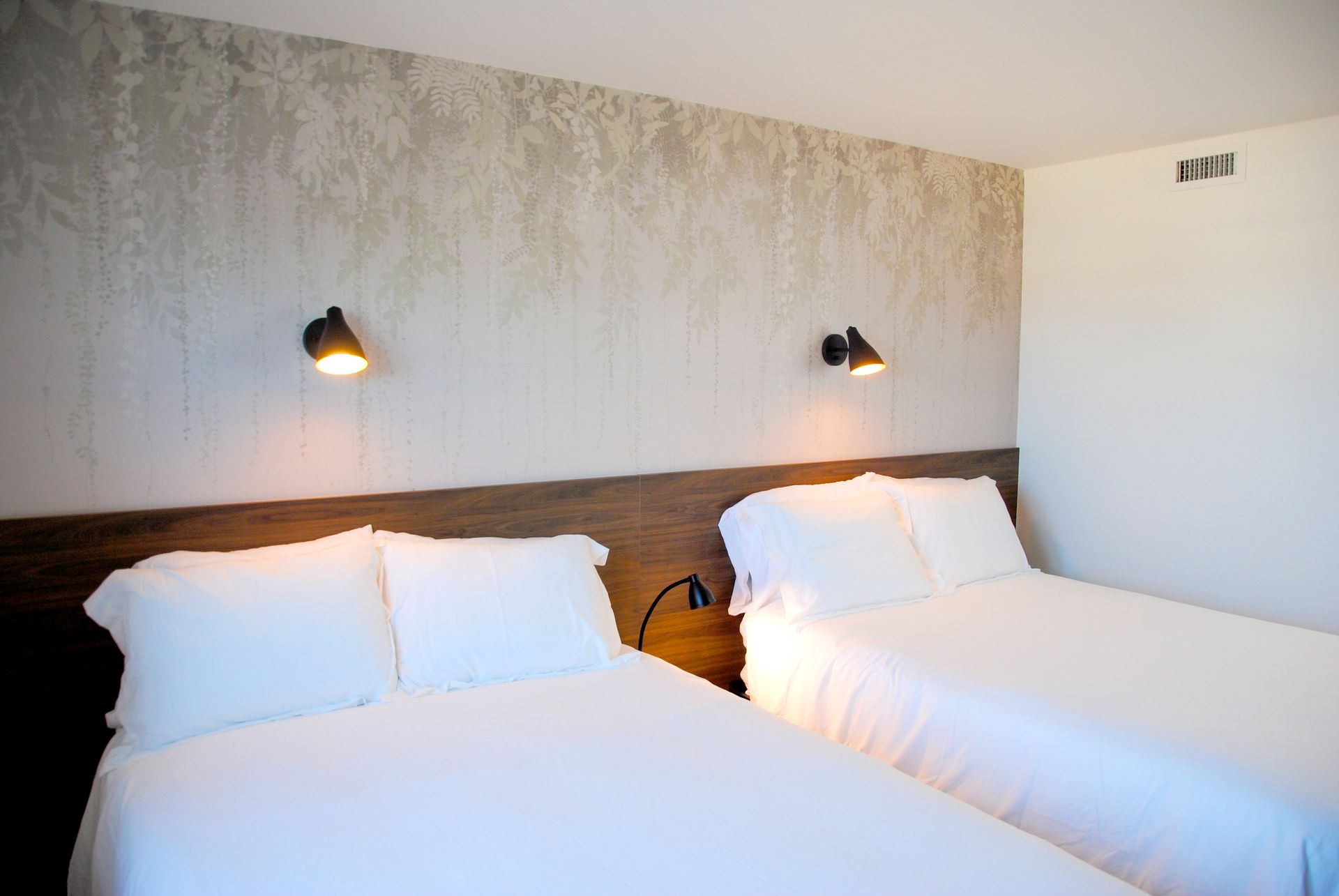 A hotel room with two beds and two lamps on the wall.